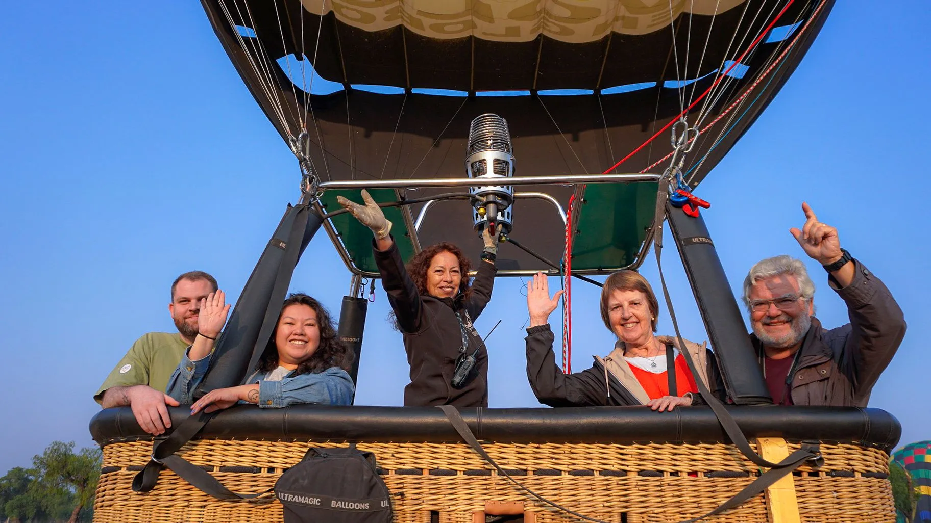Piloto y pasajeros saludando desde la canasta del globo antes del despegue